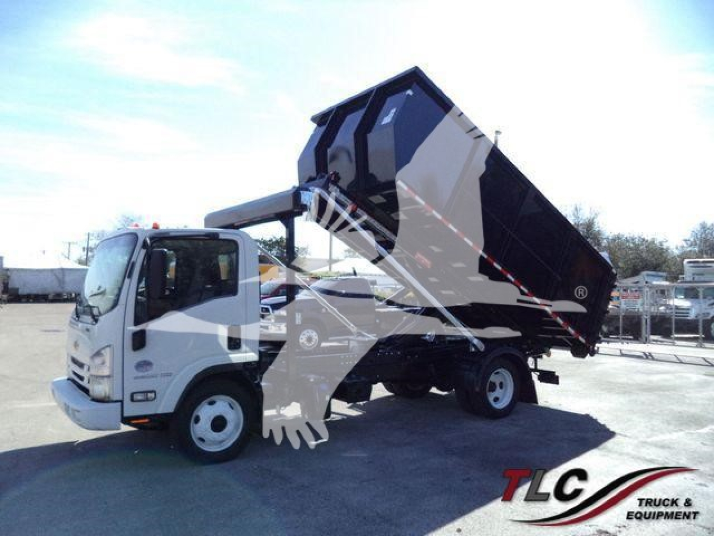 Isuzu NPR/NRR roll-off truck with dumping dump body in raised position, white cab, black and gray container, site lot in background.