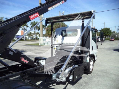 Isuzu NPR/NRR concrete roll-off truck in-service with hydraulic loader arms and chassis components visible. Includes warning labels on crane arm and utility boxes beneath the cab.