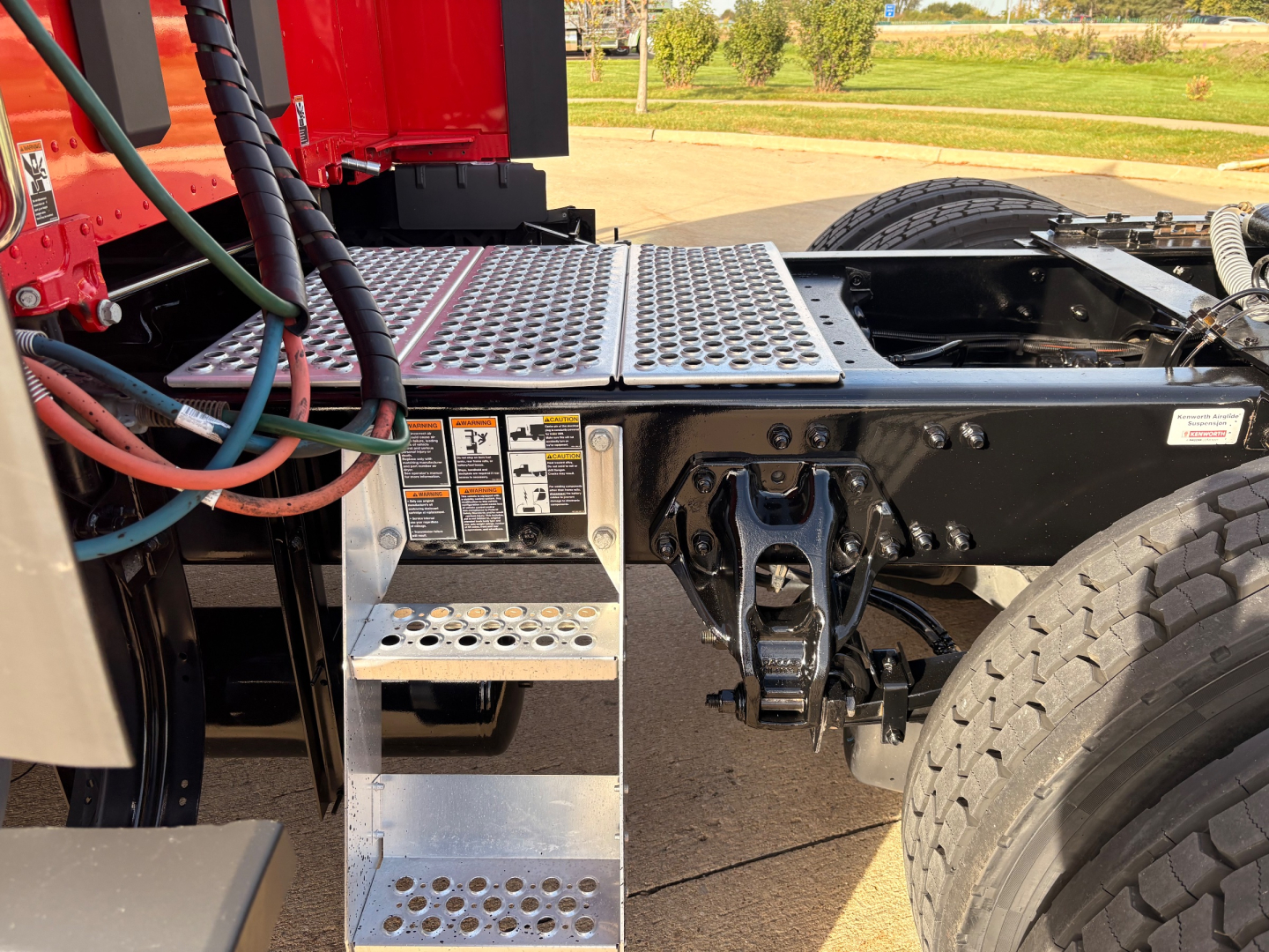 Kenworth T680 truck chassis with diamond plate steps, hydraulic lines, and rear wheel assembly visible.