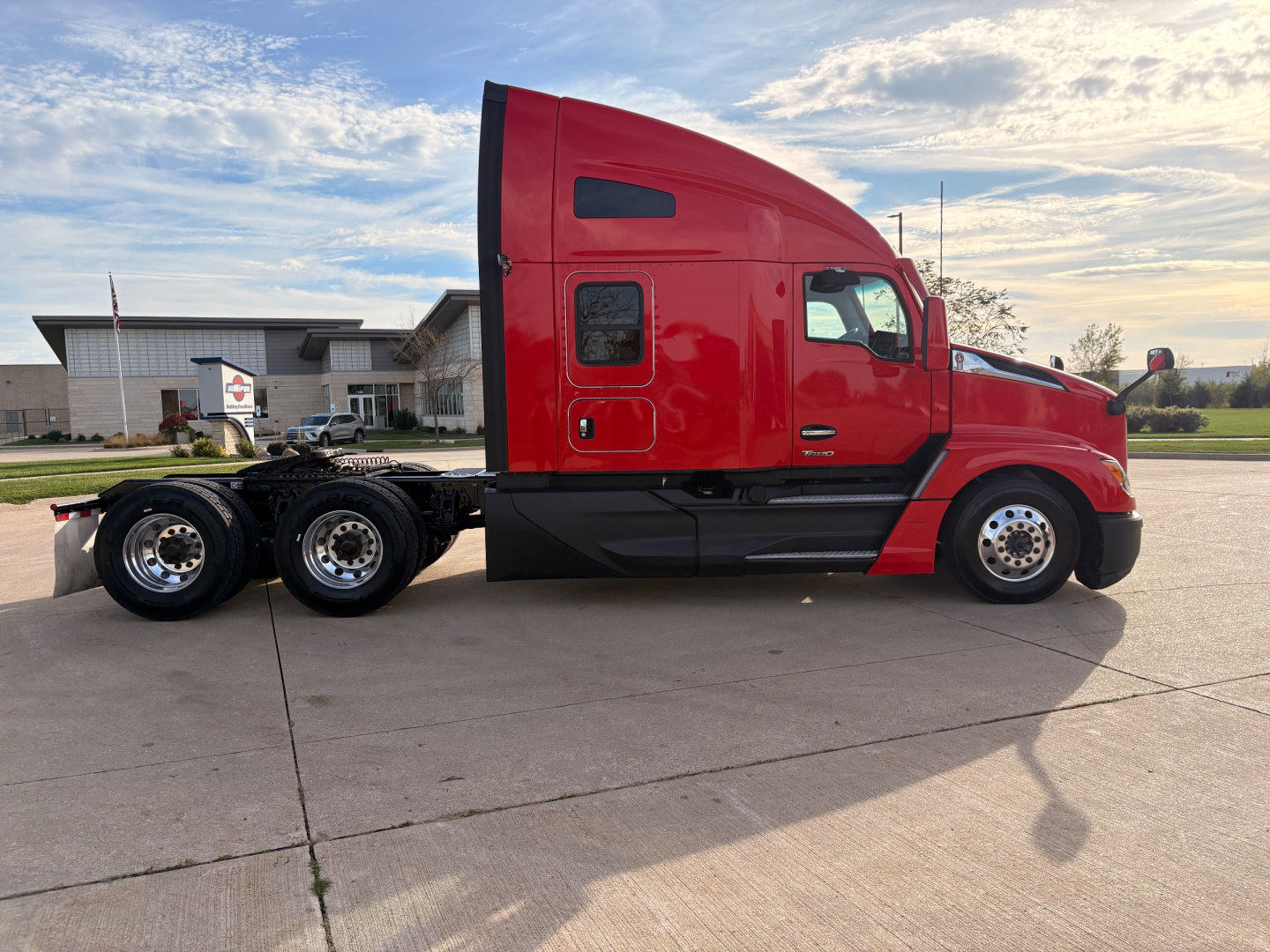 Kenworth T680 side view showing red tractor cab and black chassis with triple rear axles and wheels.