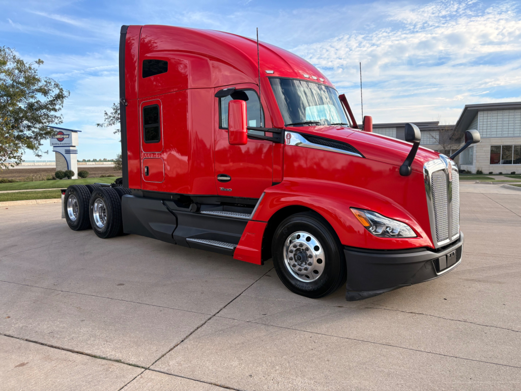Kenworth T680 conventional sleeper red truck side view showing front grille, cab, and triple rear axles with chrome wheels.