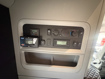 Kenworth T680 interior dash panel showing controls, a small display, and a credit card style device; air conditioning knobs and storage pocket visible.