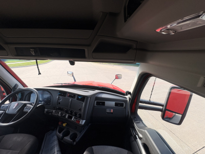 Interior of Kenworth T680 cab showing dashboard and steering wheel, with wide windshield and driver-side door mirror visible.