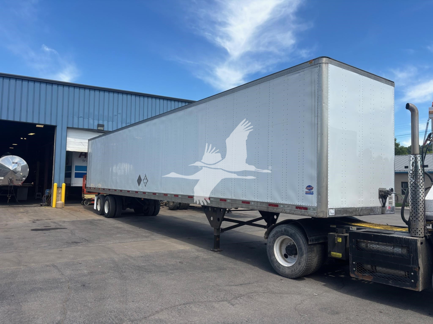 Trailer side with white bird graphic on silver 2018 Utility 4000D-X trailer, in-service, parked outside a workshop.