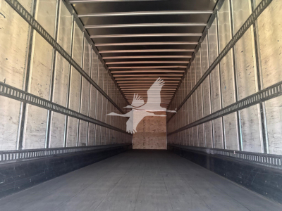 Interior of a large cargo trailer showing empty box with metal side rails and wooden front wall.