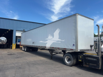 Trailer side with white bird graphic on silver 2018 Utility 4000D-X trailer, in-service, parked outside a workshop.