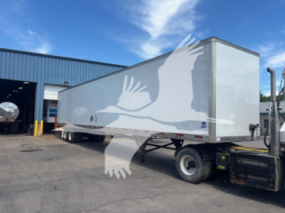 Trailer showing a white Utility 4000D-X box trailer with a graphic of birds and a blue sky reflection. Side view from front-right, parked near a service bay.
