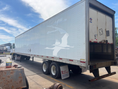 Trailer side view showing a silver Utility 4000D-X box trailer with a white bird graphic, rear doors, tandem axles, and a drop ramp.