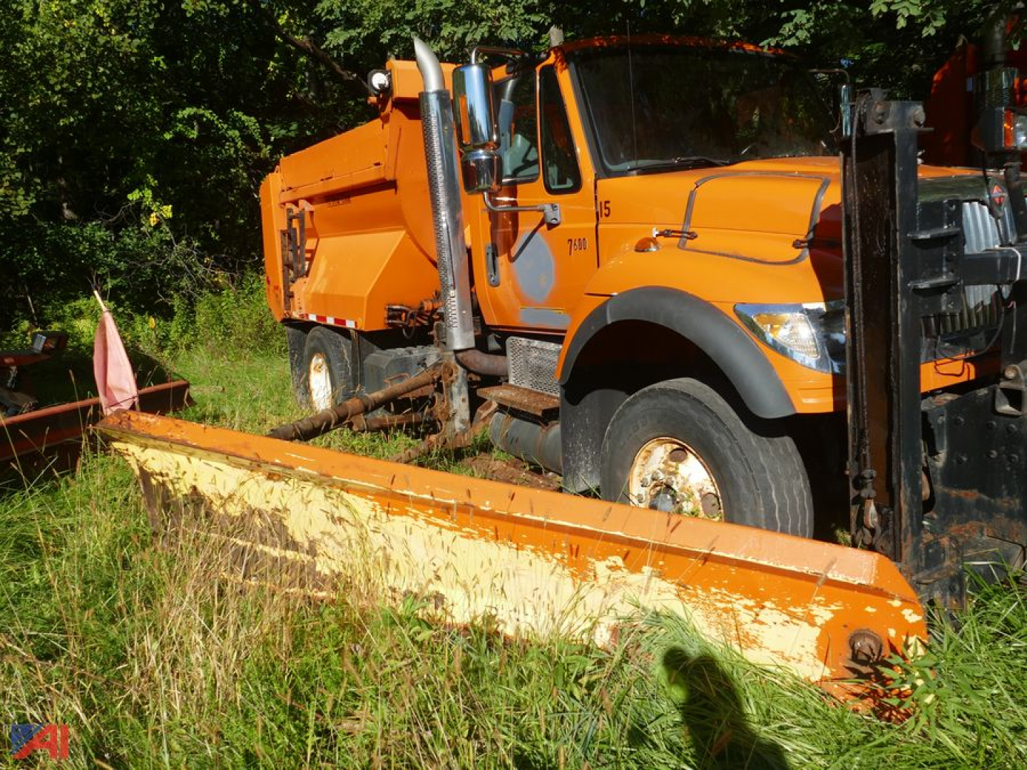 Orange dump truck with wing showing side view and snowplow blade in foreground