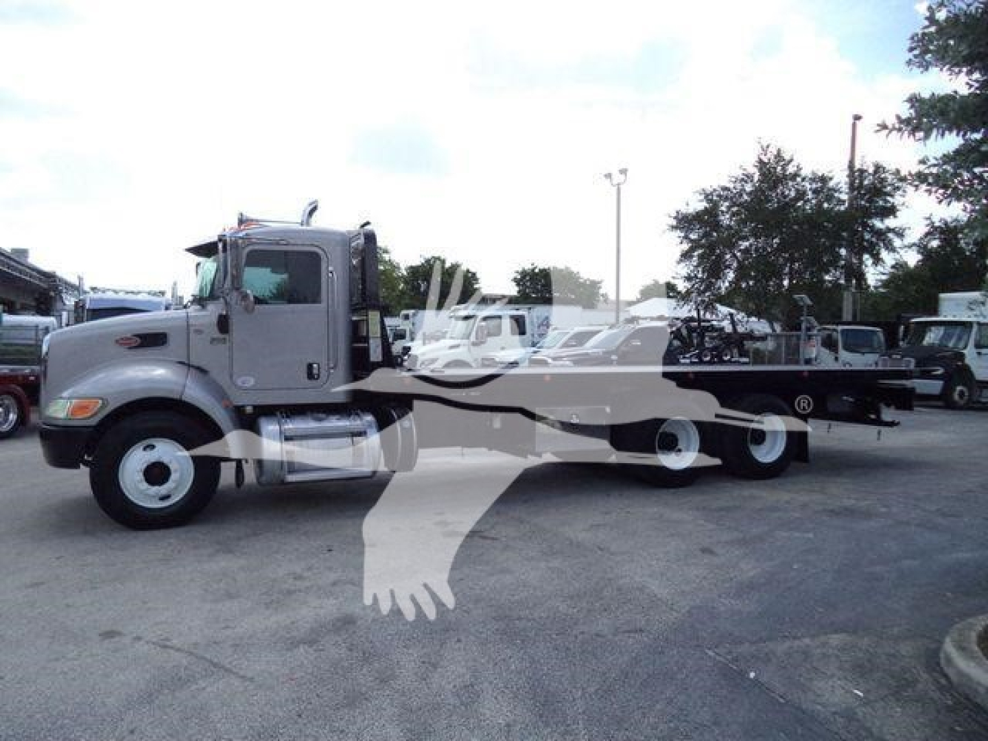 Peterbilt 348 rollback truck side view with extended flatbed and wheel lines in a dealership lot.