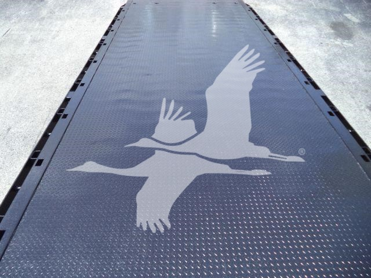 Image shows a large metal flatbed/rollback deck with a large logo of two birds in flight. No cab, only the deck surface visible.