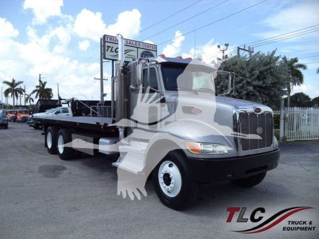Peterbilt 348 rollback truck in sight showing front cab and long flatbed with two rear axles; 2015 model, white and gray color, dealership lot in background.