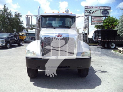 Peterbilt 348 rollback truck front view showing large grille, bumper, headlights, and side mirrors in a dealership lot.