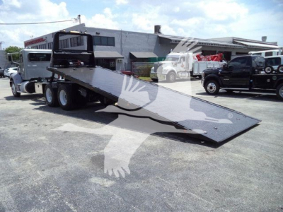 Peterbilt 348 rollback truck with a lowered flatbed in an outdoor lot, showing a black steel ramp and dual rear axles.