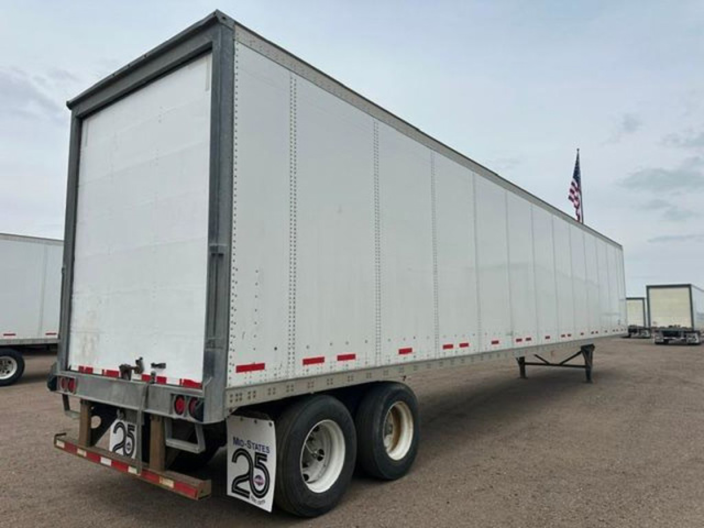 Semi-trailer van showing dual rear wheels and aluminum side panels with red and white reflectors along the lower edge.