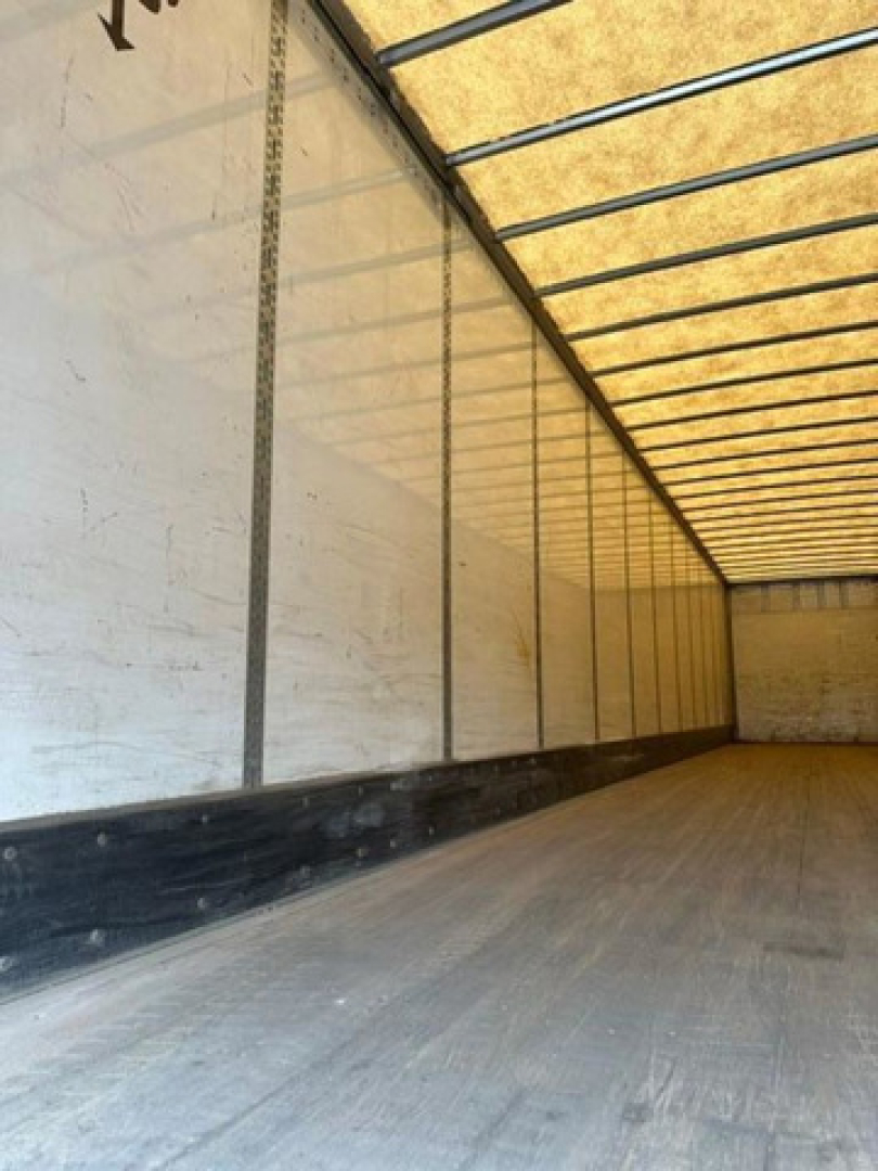 Trailer interior showing cargo space with metal plated walls and wooden roof support, empty floor.
