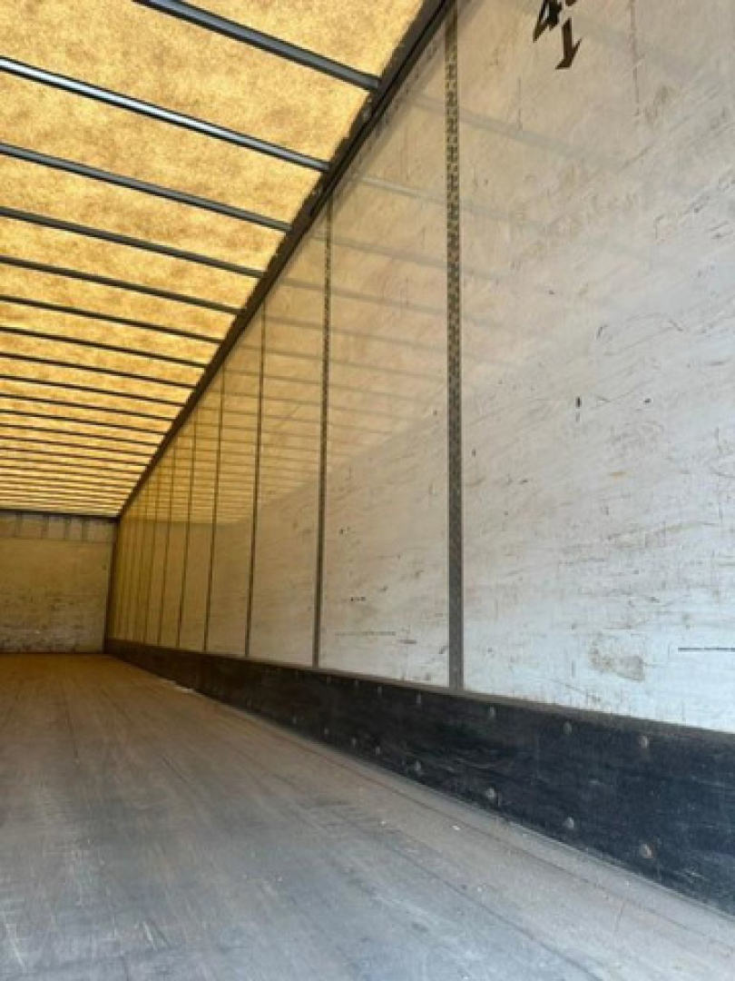 Trailer interior showing empty cargo space with wooden floor and white side walls; overhead ribs and roof panels visible.