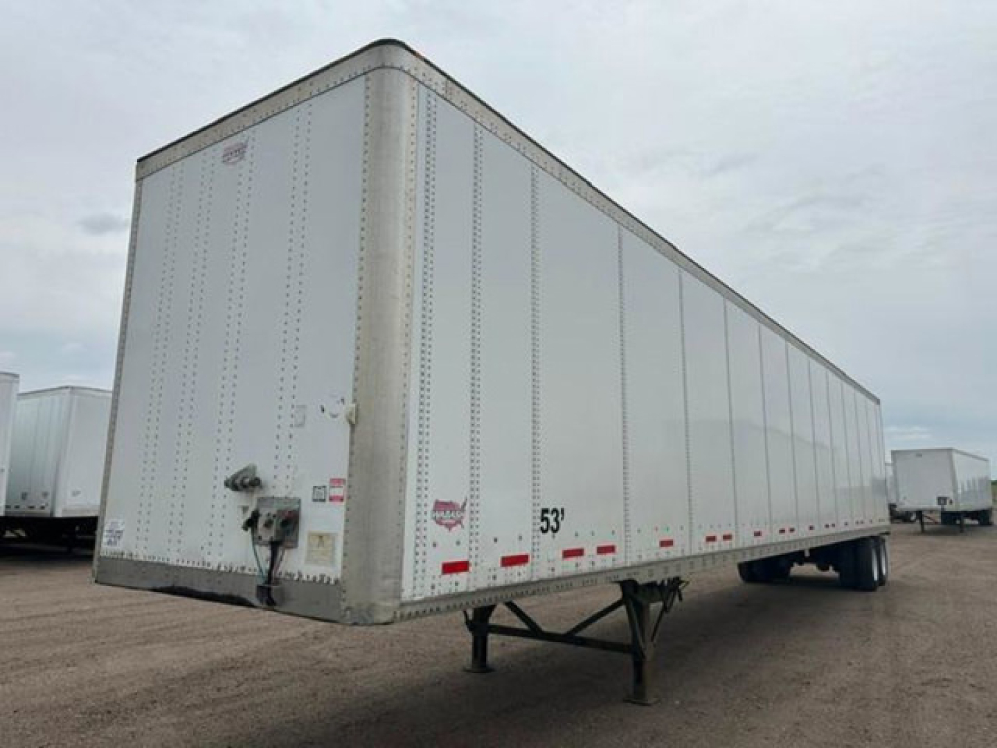 Trailer side view showing a white Wabash semi-trailer with front hitch and side rails; visible are red/white reflective markings and a wheel-less front with landing gear.