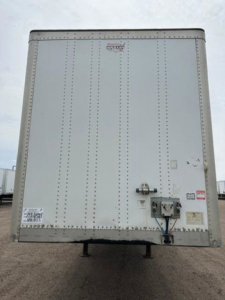 Trailer rear door with hitch and wiring showing vertical riveted panels and small stickers on lower left; rear view of a used 2014 Wabash van trailer.