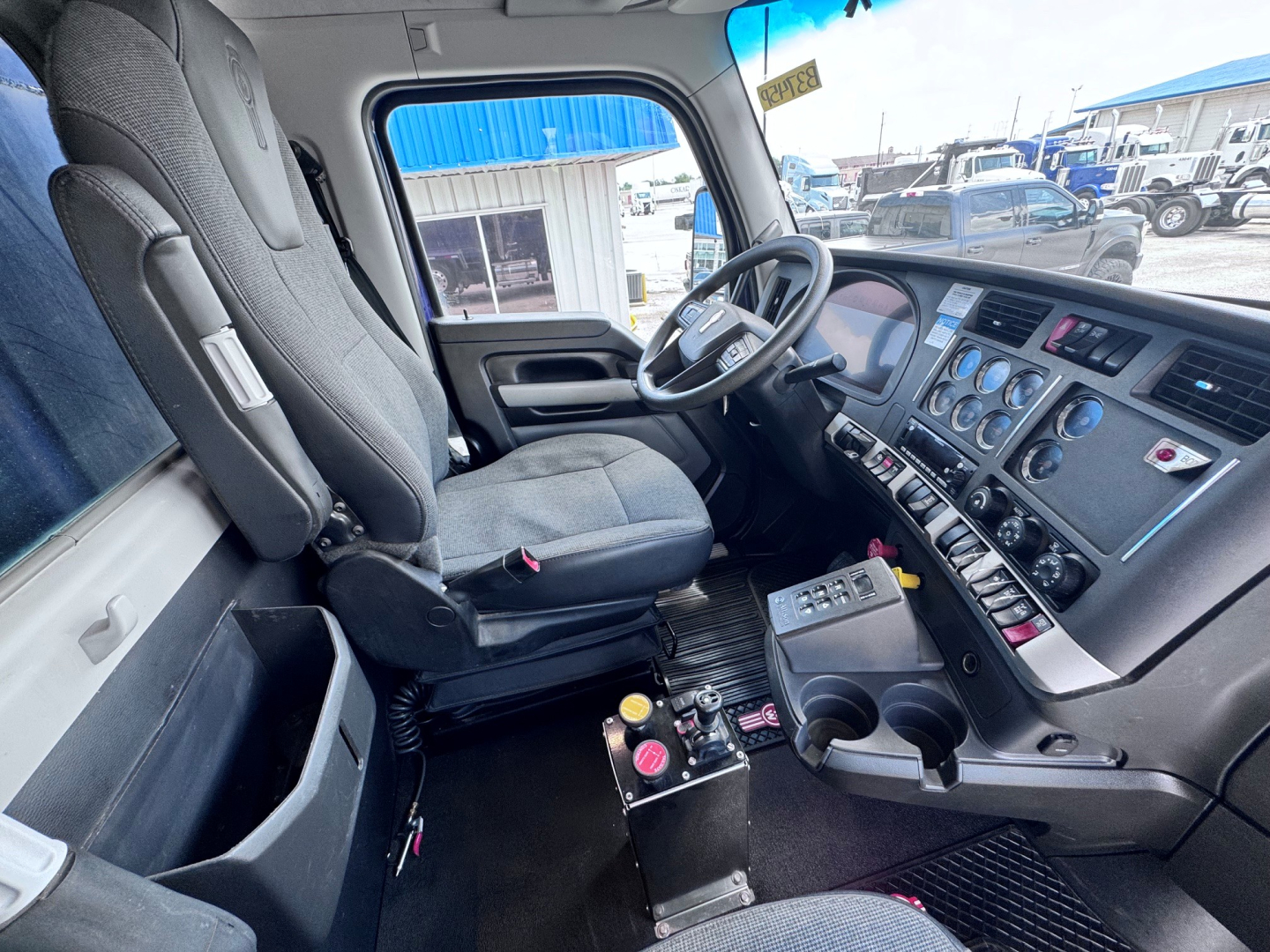 Truck cab interior of a Kenworth T880 showing driver seat, steering wheel, dashboard with gauges, center console, and control panel.