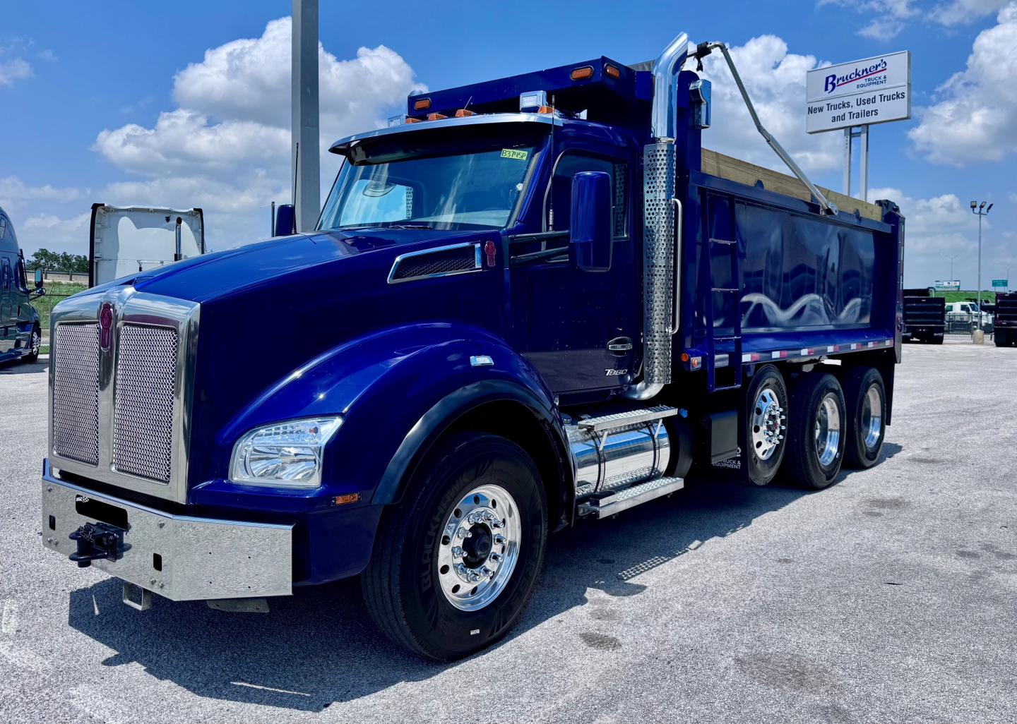 Kenworth T880 dump truck with blue paint and chrome grille, side view showing dual rear axles and dump bed.