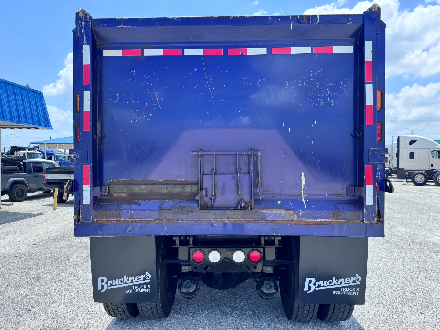 Dump truck tail showing rear bed with blue bed, bumper with red/white reflective strips, and mud flaps reading Bruckners Truck Equipment.
