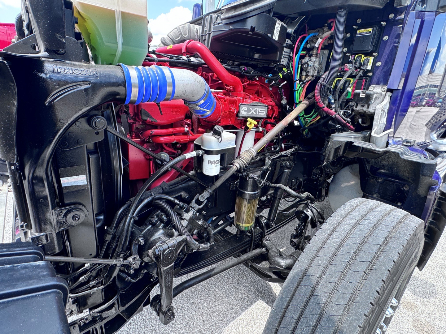 Kenworth T880 engine bay showing red engine block, blue turbo hose, white DEF/Filter canister, and multiple hydraulic lines.