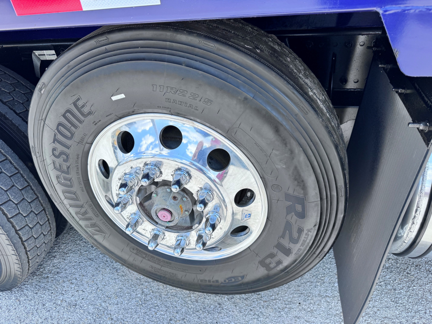 Wheel close-up on blue Kenworth T880 dump truck showing Bridgestone tire and chrome steel rim with lug nuts.