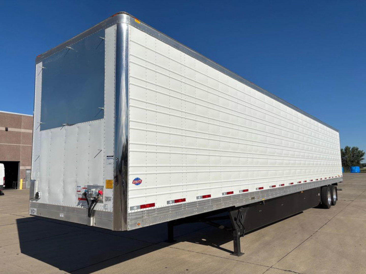 Utility refrigerated trailer in side view showing aluminum exterior and rear doors with hitch, jack, and wheel area.