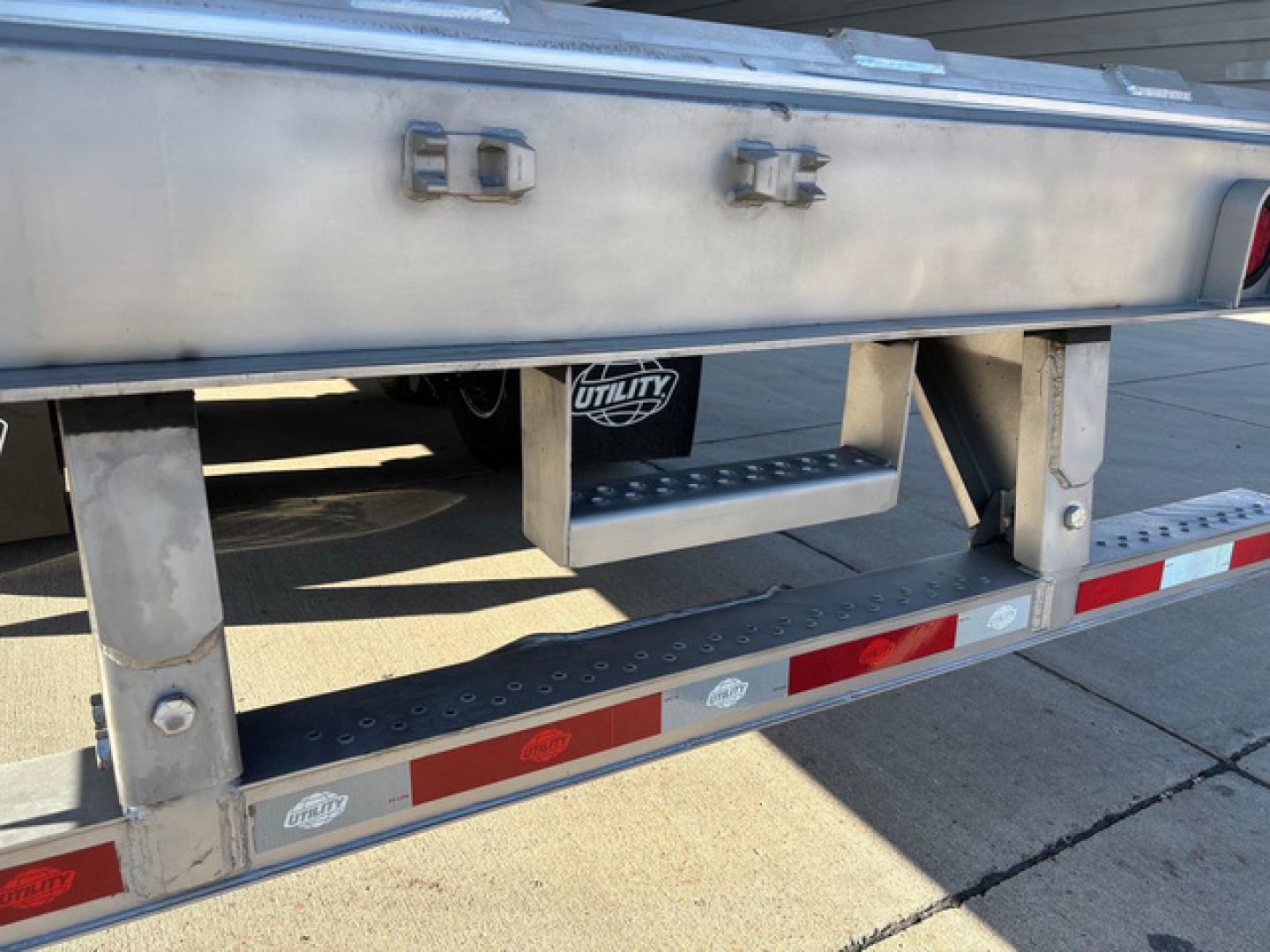 Trailer hitch area of a 2027 Utility refrigerated trailer showing stainless steel frame and steps, stock decals, and utility brand badge.