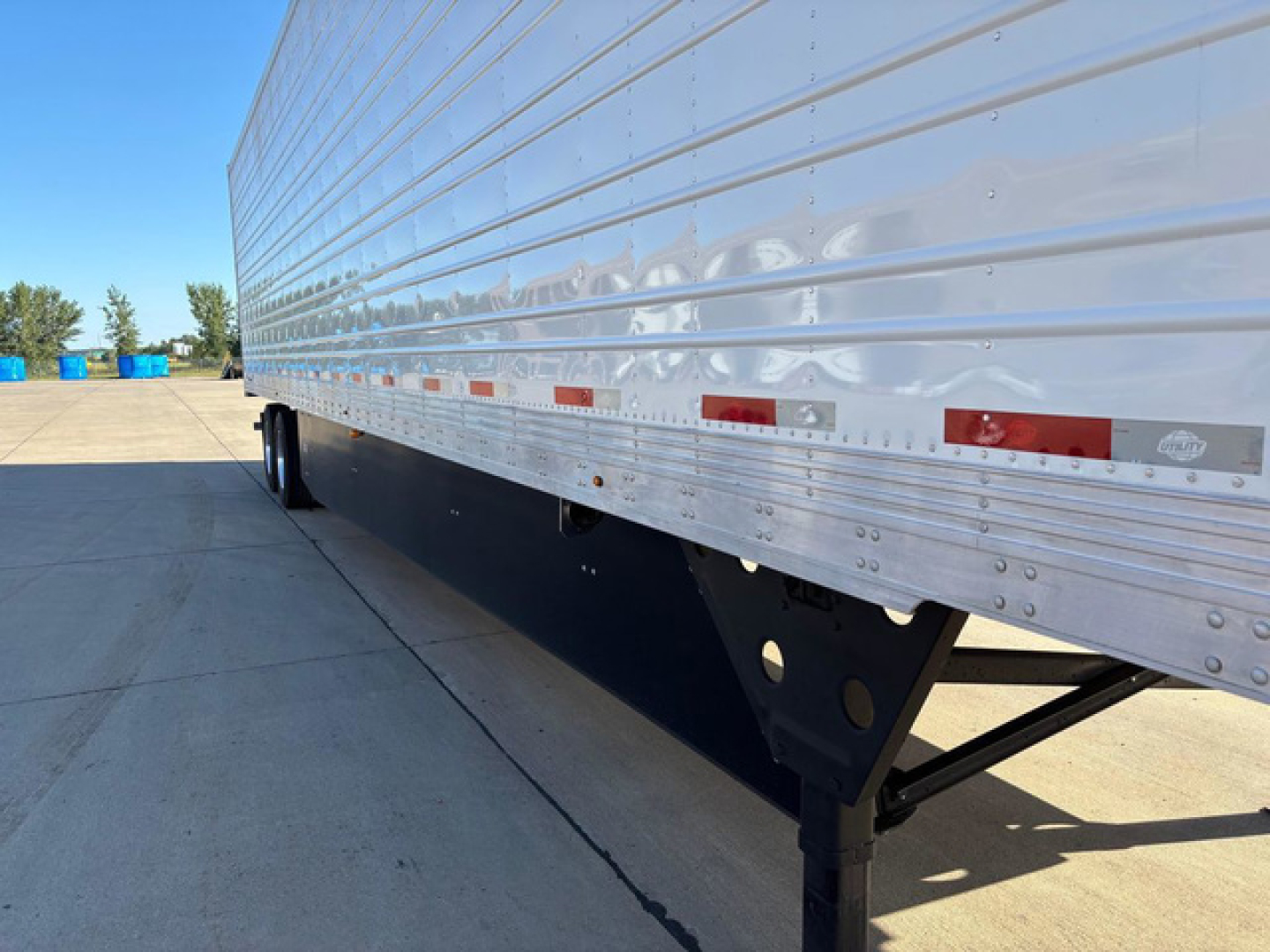 Trailer side view showing aluminum refrigerated trailer with reflective lower panel and undercarriage support beams.