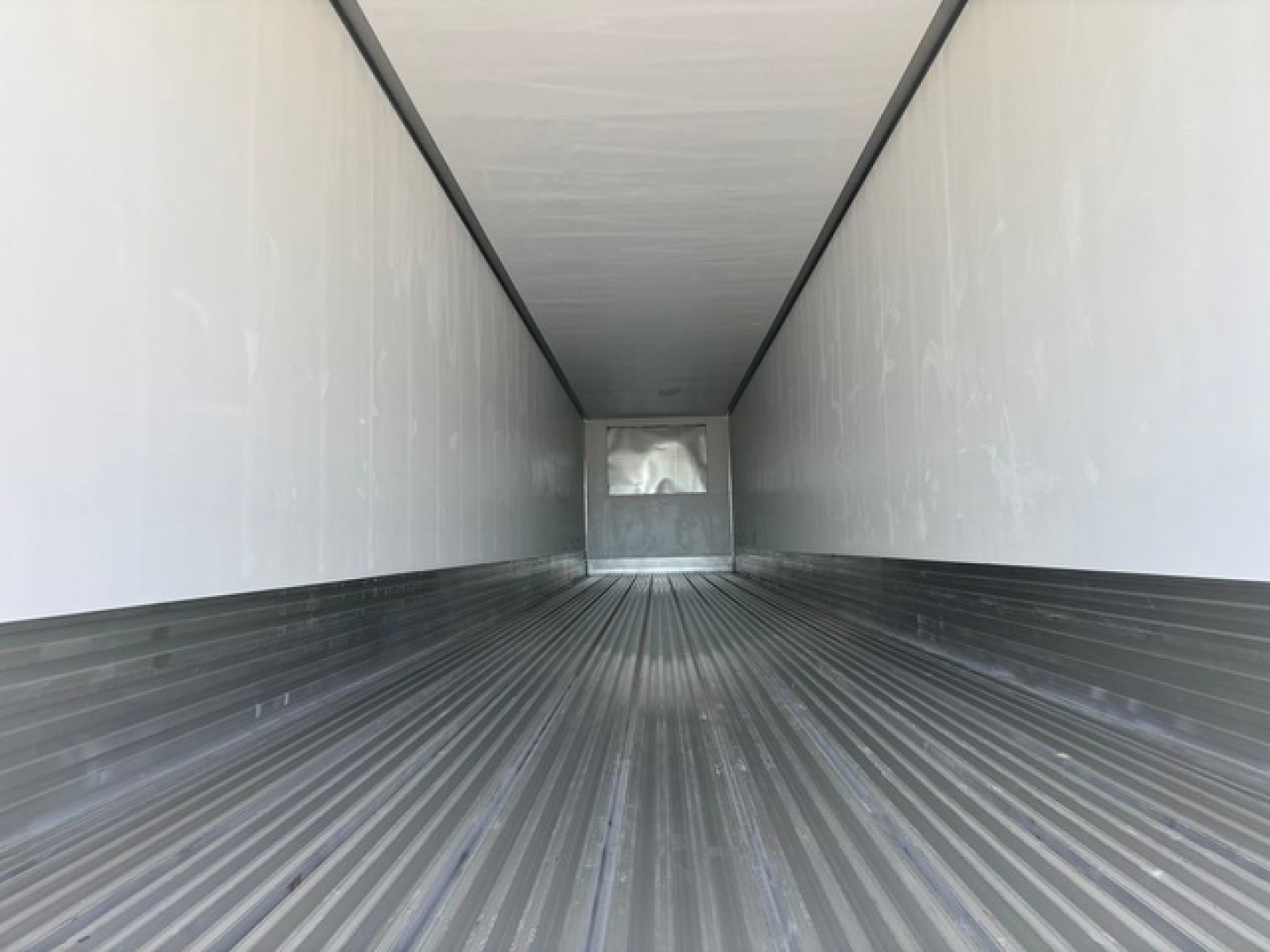 Trailer interior showing empty refrigerated cargo area with ribbed metal floor and white side walls, leading to a rear door.