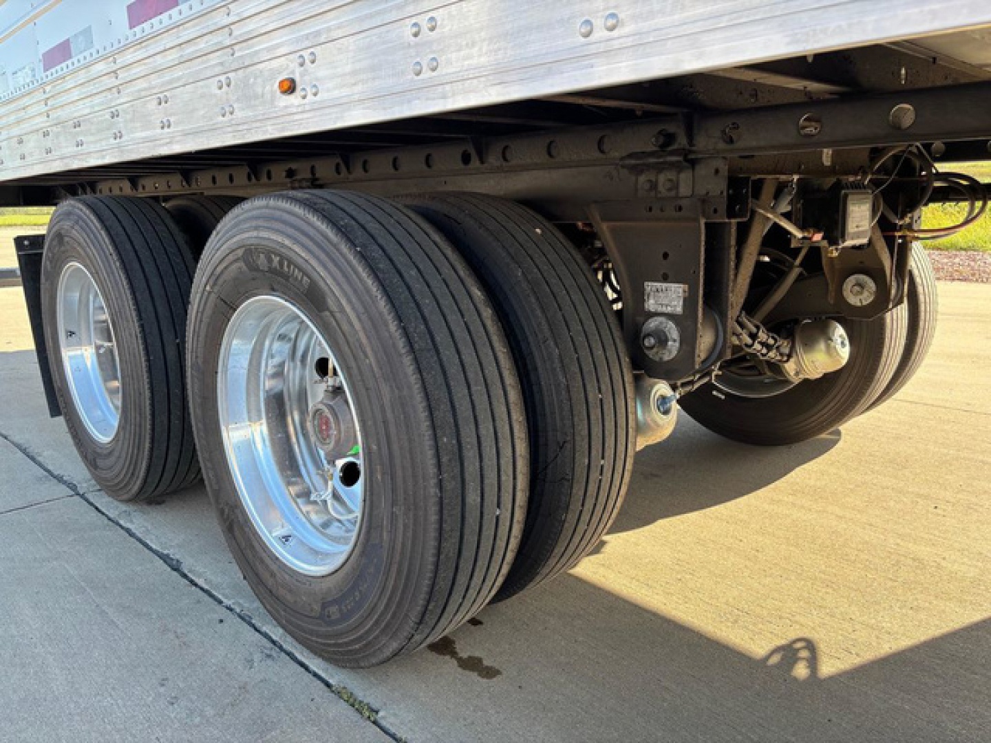 Trailer axle group of a 2027 Utility Reefer showing dual rear axles and chrome rims with black tires, undercarriage with suspension and wiring visible.