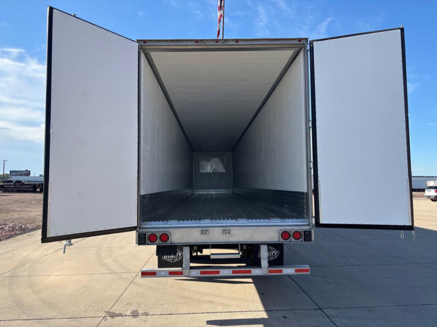 Utility reefer trailer rear view with doors open showing empty refrigerated cargo area and metal floor.