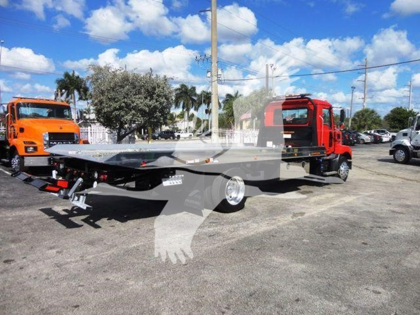 New 2027 Mack MD6 rollback truck with a flatbed, red cab, and orange truck in background showing side view.