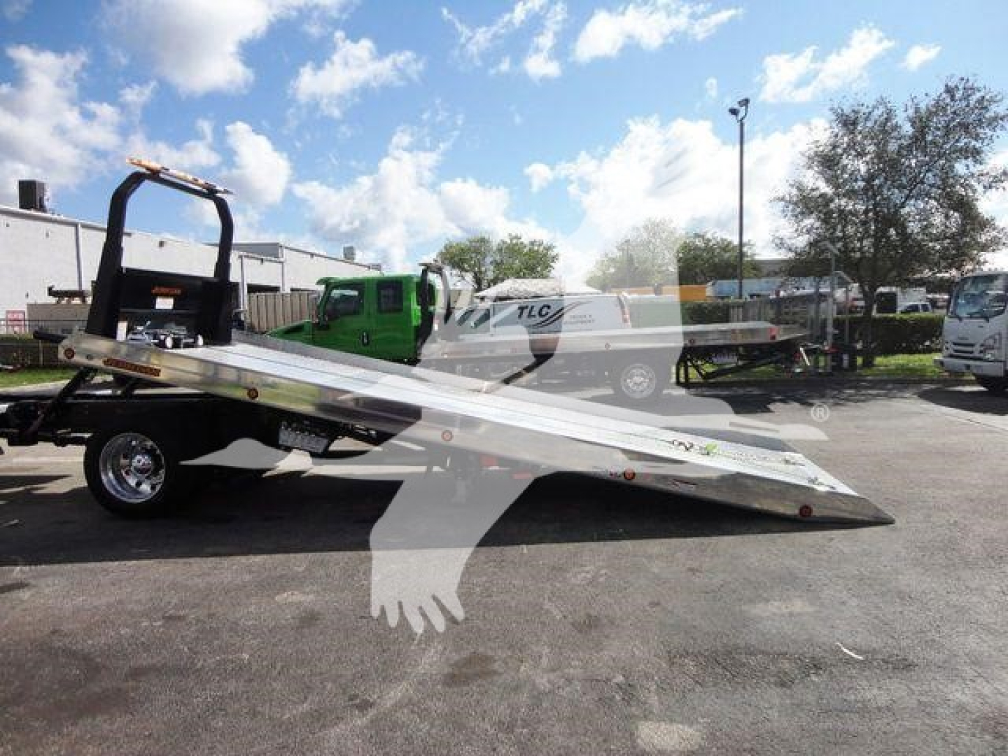 Flatbed rollback tow truck on trailer showing hydraulic tilt bed and ramps.