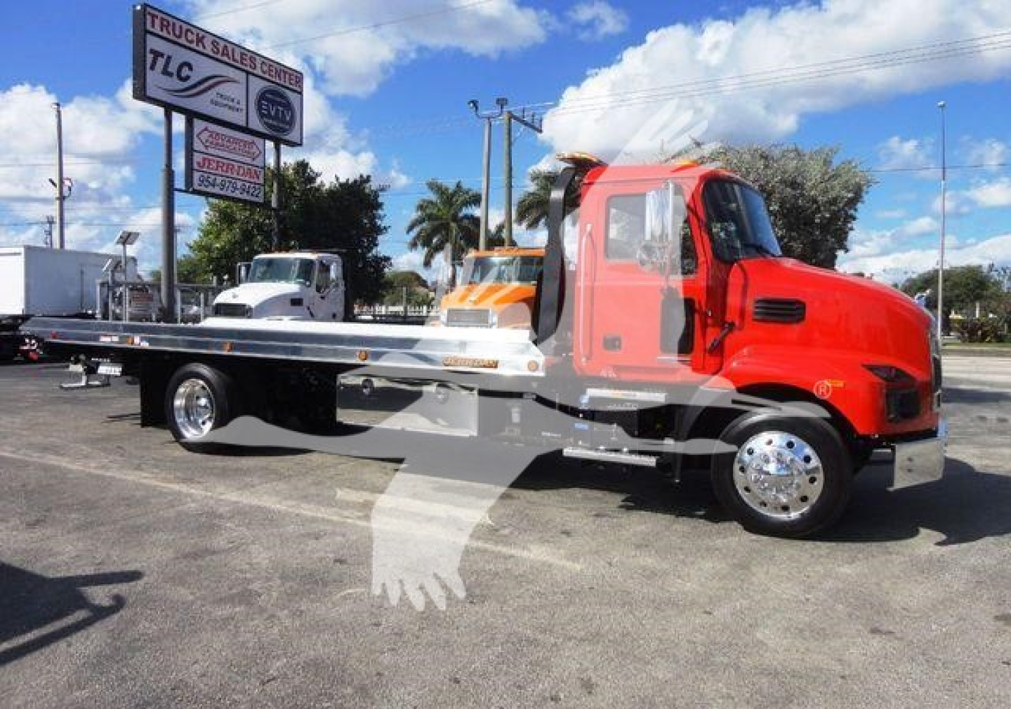Truck bed with red 2027 Mack MD6 rollback wrecker body in a dealership lot showing flatbed and chrome wheels.