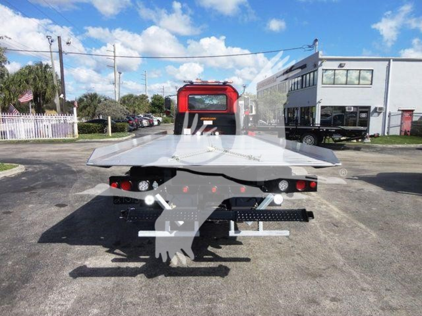 Flatbed tow truck back view with red cab and metal platform, tail lights visible.
