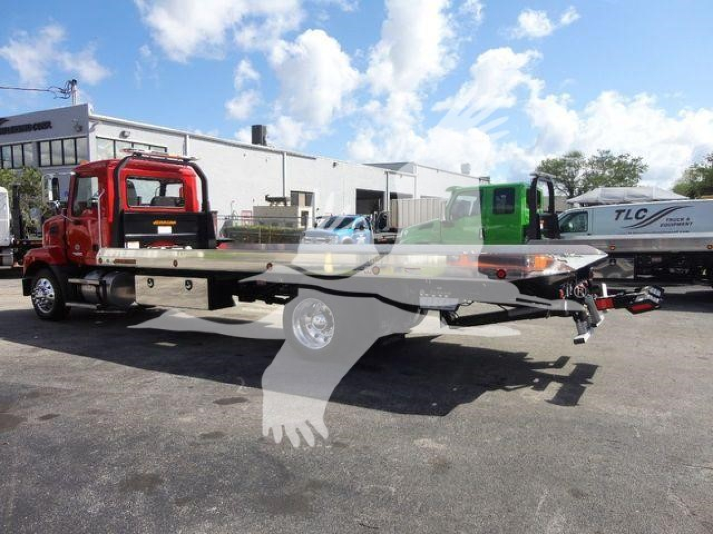 Mack MD6 rollback truck with red cab and flatbed, side view, showing the vehicle in a dealership lot.