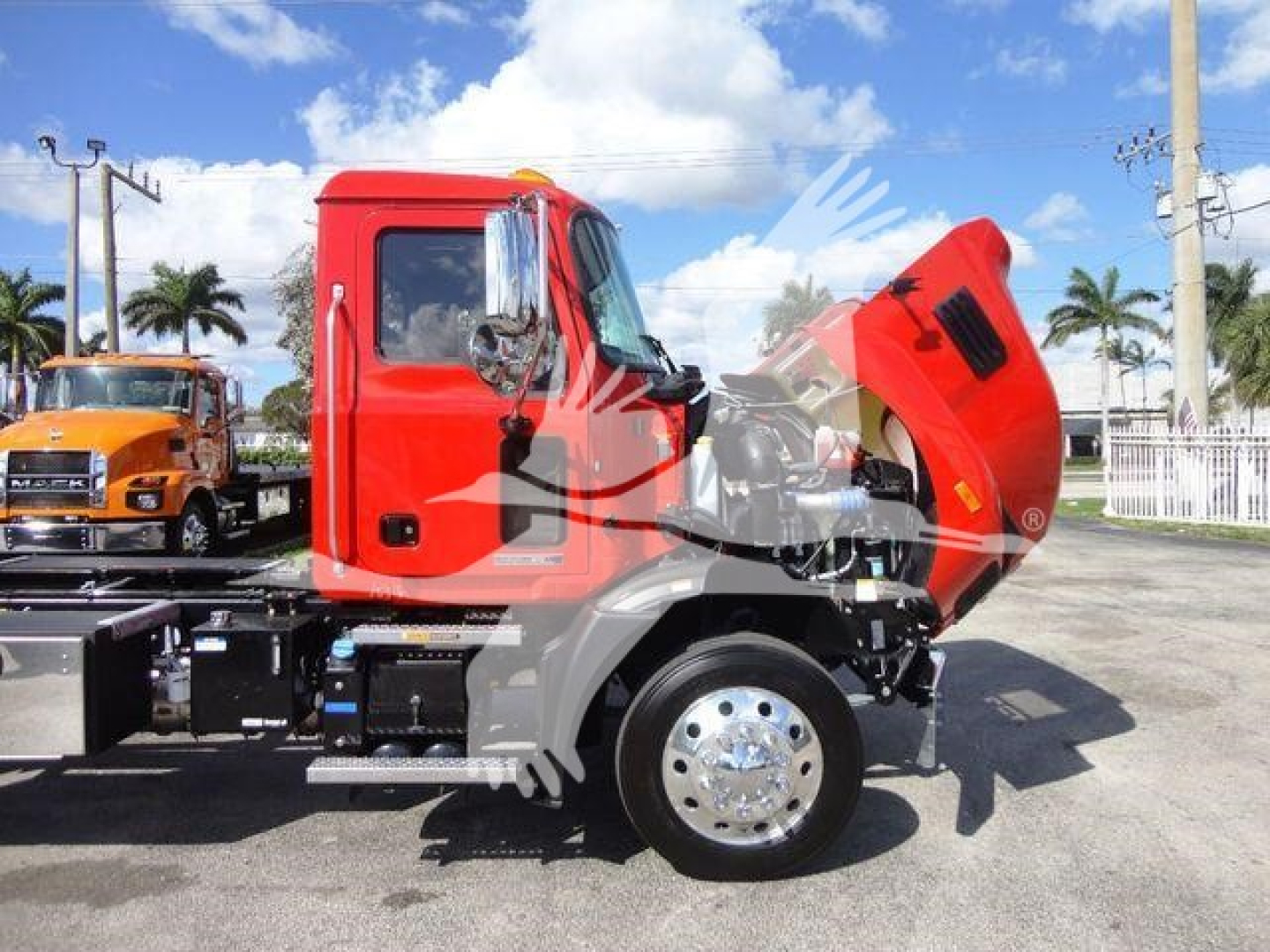 Mack MD6 truck side with hood raised showing engine area and cab in red, front wheel visible, on a dealership lot.