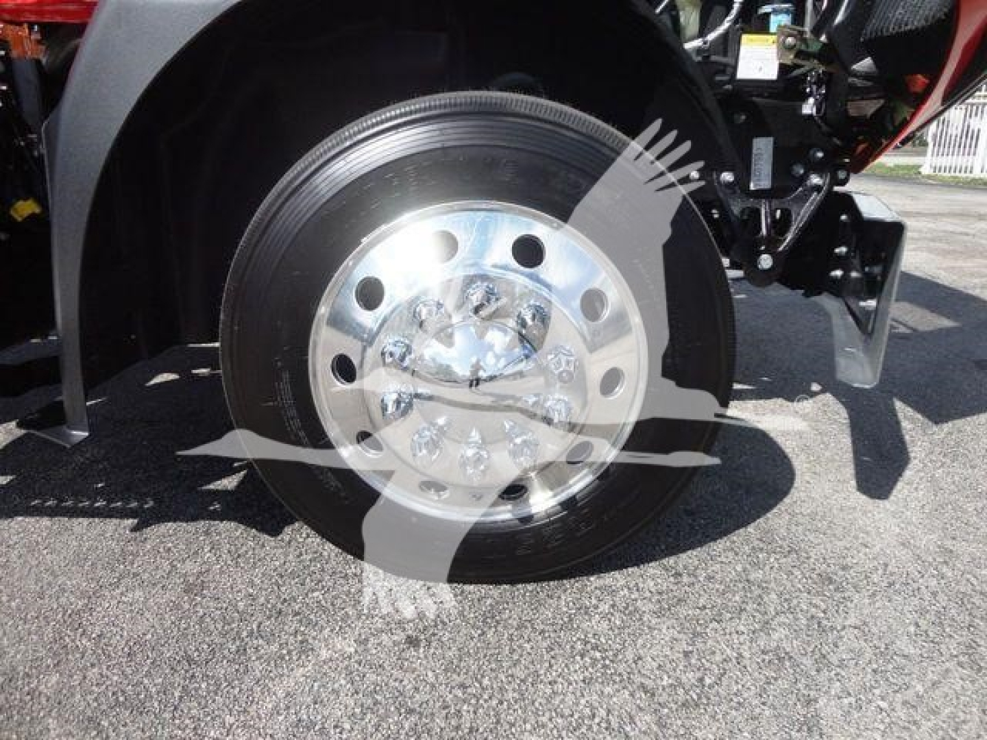 Front wheel and chrome hub of a Mack MD6 rollback truck showing polished steel wheel with lug nuts and tire, partial view of suspension and fender