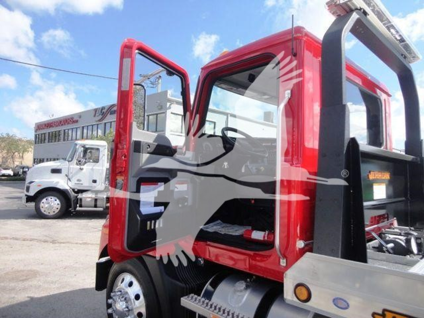 MD6 truck cab side view showing open door and red body, Mack MD6 rollback equipment, chrome wheels, with another white truck in background.