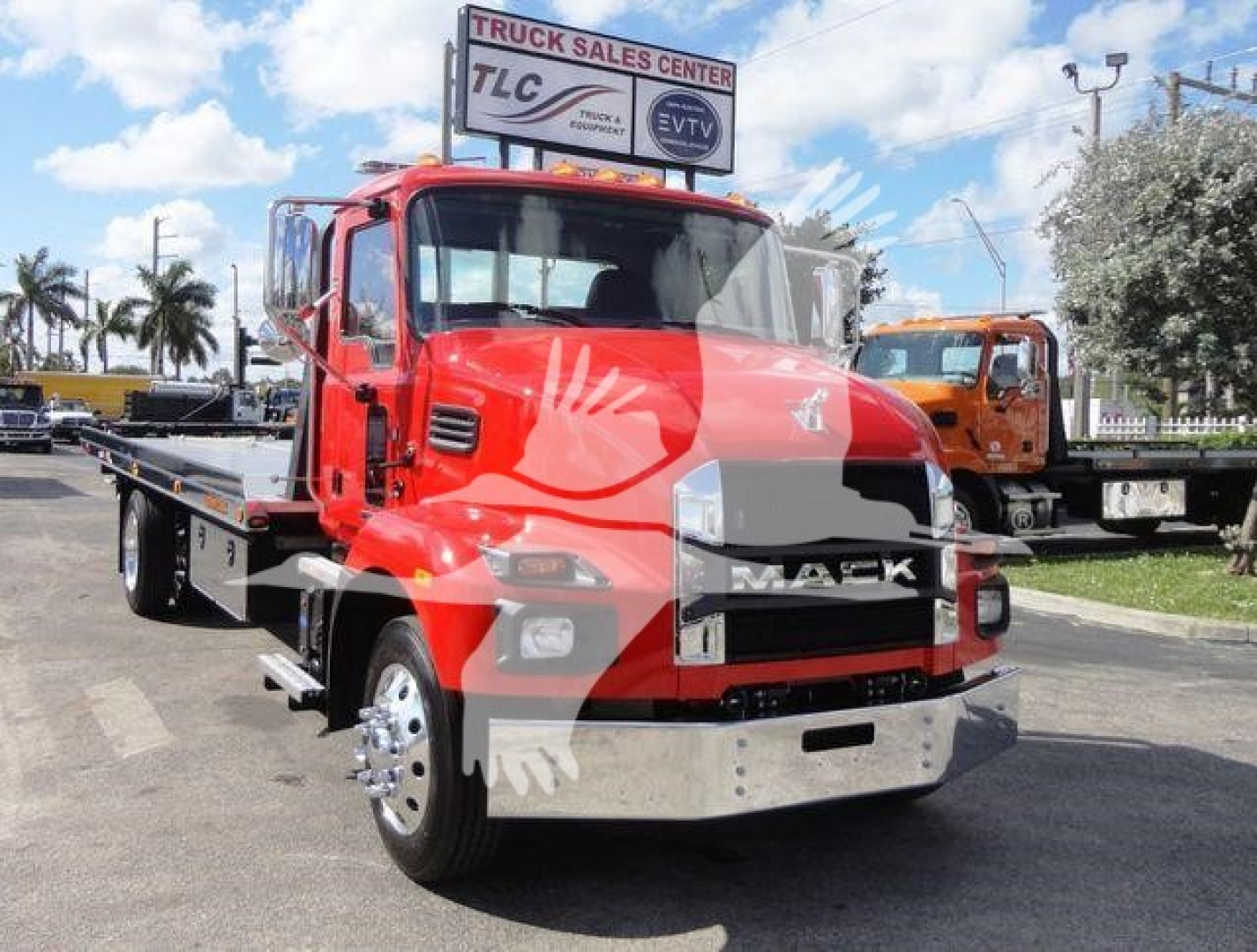 MD6 Mack rollback truck in showroom stance with bright red cab and flatbed, front view showing chrome bumper and Mack grille, dealership sign in background.