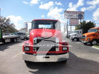 Front view of a red Mack MD6 truck in a dealership lot with other trucks and a sign in the background.