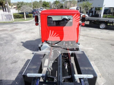 Front view of a red 2027 Mack MD6 truck cab and chassis showing the back of the cab and the frame rails for a rollback configuration.