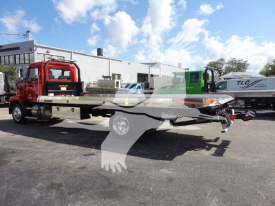 Mack MD6 rollback truck with red cab and flatbed, side view, showing the vehicle in a dealership lot.