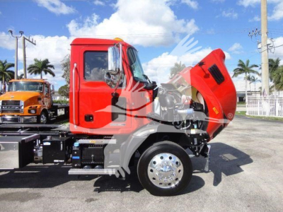 Mack MD6 truck side with hood raised showing engine area and cab in red, front wheel visible, on a dealership lot.