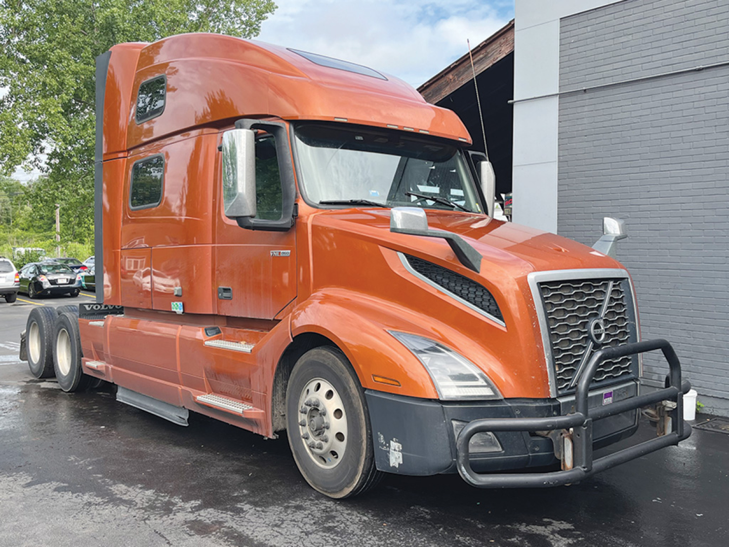 Volvo VNL 860 sleeper cab truck in orange, front three-quarter view, showing chrome grille guard and aerodynamic hood, dual rear axles, and side mirrors.