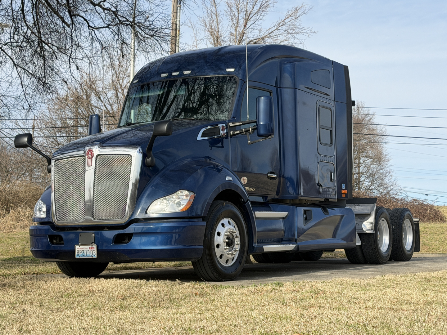 Kenworth T680 conventional sleeper tractor in dark blue, front three-quarter view with chrome grille and dual rear axles.