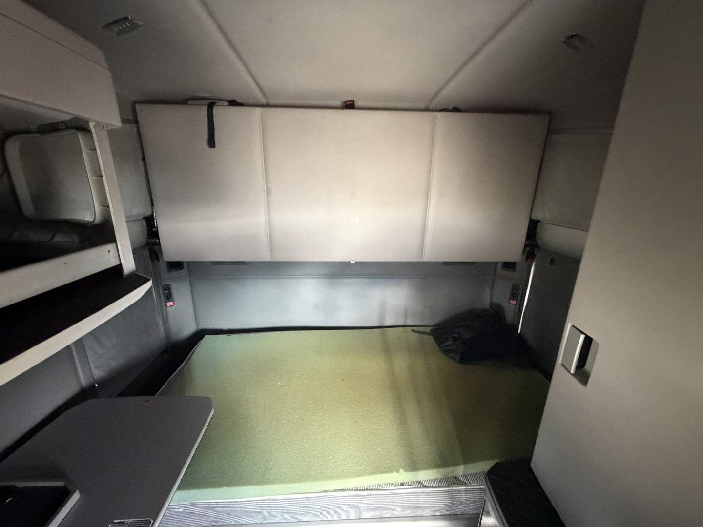 Cab interior of a 2020 Kenworth T680 sleeper truck showing a cargo area with a green floor, side cabinets, and a rear bulkhead.